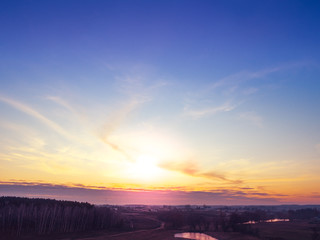 Magical sunset in the countryside in autumn. Rural landscape in the evening. Aerial view of brook, village and arable fields. Panoramic view