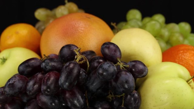 Grapes, apples, grapefruit and orange rotate clockwise on a black background, side view