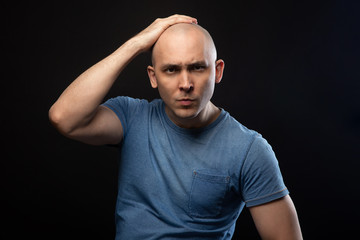 Portrait of bald man in blue tee shirt with hand on head