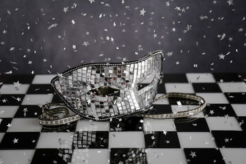 Maschera d'argento sopra la scacchiera bianca e nera con coriandoli  e cristalli