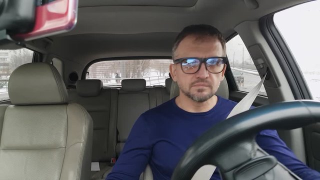 Bearded man in blue clothes wears glasses and starts drive car