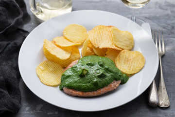 grilled hamburger with green sauce nd potato chips on white plate