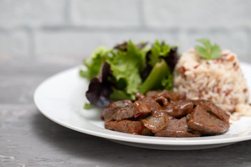 fried liver with salad and boiled rice on white plate