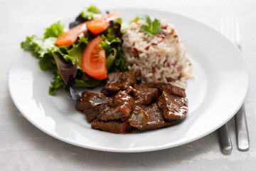 fried liver with salad and boiled rice on white plate
