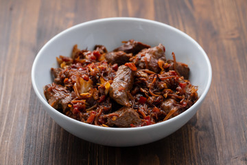 meat with vegetables in white bowl on brown wooden background
