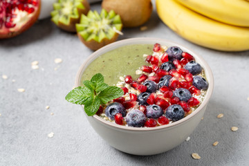 Green smoothie bowl with banana, kiwi, blueberry, granola and pomegranate. Healthy Breakfast detox cocktail in a bowl, vegan food. 