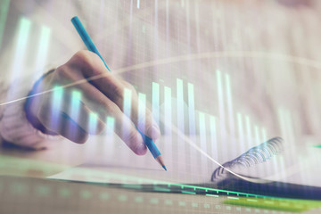 Financial forex graph displayed on hands taking notes background. Concept of research. Double exposure