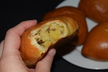 Someone is holding a nibbled homemade pie with potatoes and pies on a white plate on a black background. Close up.