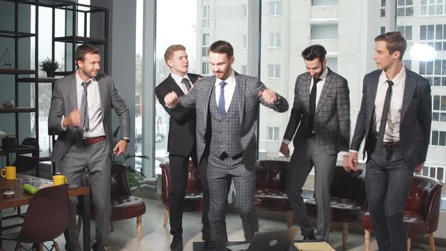 Happy positive cheerful business team dance after meeting, celebrate in office. Everyone in elegant tuxedo.