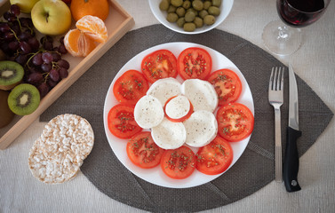 Stay fit with a light and healthy dish with tomato and mozzarella. Accompanied by rice cakes, green olives and fruit. A glass of red wine