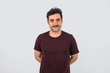 Portrait of brown, smiling, handsome man with mustache and purple t-shirt standing looking at camera. Gray background.