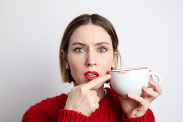 Young woman with negative face showing lipstick mark on her cup. Isolated on white background.