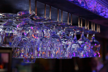 Empty wine glasses hanging over a bar rack in a nightclub.