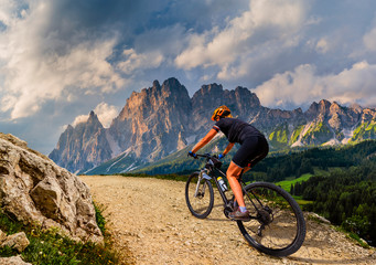 Fototapeta na wymiar Tourist cycling in Cortina d'Ampezzo, stunning rocky mountains on the background. Woman riding MTB enduro flow trail. South Tyrol province of Italy, Dolomites.