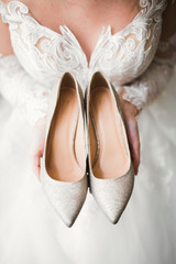 Beautiful luxury bride in elegant white dress holds wedding shoes in the hands