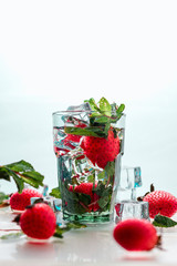 strawberries fall into the water. The freshness of the water. A glass of water and ice.  Fresh strawberries in water. Clean water in a glass. Cocktail with ice.