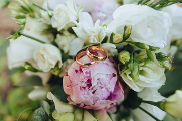Wedding gold rings close-up on a background of pink, white peonies and roses. Photography, concept.