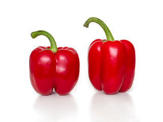 Two red bell peppers with green cuttings on a white background
