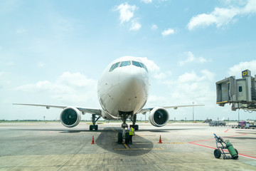 technician or engineer safety check of modern passenger or cargo airplane parking at terminal gate of international airport on a cloudy blue sky background