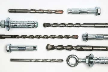 Set of drill bits and anchor bolts on a white background.  The mounting tool for fixing lies in several horizontal rows.