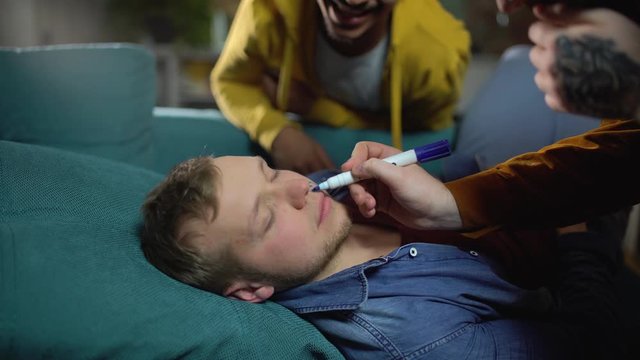 Male friends pranking their sleeping buddy after alcohol party, student life