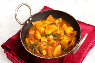Homemade Indian spicy Potato and tomato curry also known as aloo tamatar ki sabji in hindi, served in iron kadai with smiling spatulas. Copy Space.