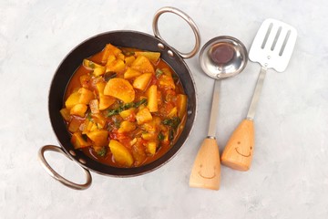 Homemade Indian spicy Potato and tomato curry also known as aloo tamatar ki sabji in hindi, served in iron kadai with smiling spatulas. Copy Space.