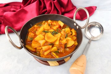 Homemade Indian spicy Potato and tomato curry also known as aloo tamatar ki sabji in hindi, served in iron kadai with smiling spatulas. Copy Space.