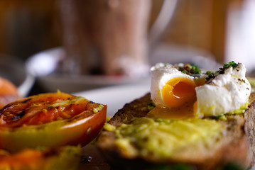 Poached egg on toast, with smoked salmon, avocado, grilled tomato, and baby spinach on wooden table in a street cafe