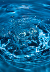 Fototapeta na wymiar water drop splash in a glass blue colored. Fresh liquid concept. Close up.