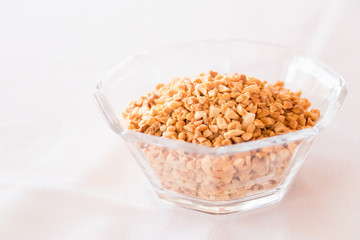 Glass bowl of roasted crushed peanuts isolated on white background.