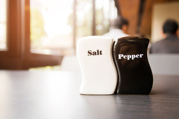 Ceramic salt and pepper shakers on wooden table at restaurant background.