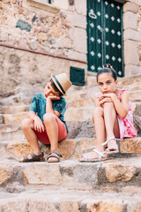 Two bored children sitting on a stairs on a summer day