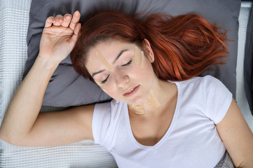 Naklejka premium Kineyzio tape on the face of a sleeping girll. A woman lies in a bed with patches for facial rejuvenation.