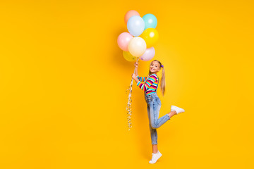 Full body photo of positive cheerful kid have birthday catch many air baloons flying air in sky wear jeans sweater sneakers isolated over bright color background