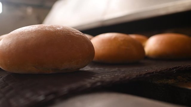 fresh hot bread comes out of the oven in close-up on a conveyor belt and is sprayed with water to add gloss and Shine against the background of a bakery manufacturer or factory..