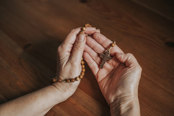 Woman praying with wooden rosary, religion concept