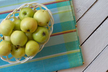 Fresh, ripe Apple harvest. Nature theme with green apples in a white basket on a wooden background. The concept of the nature of the fetus. Top view with space for text