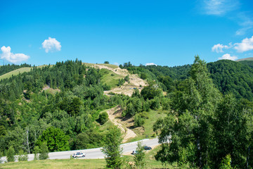 a large hill covered by pine forests near the mountains. A beautiful blue sky. Tourists stopped on the road to admire the scenery. the road crosses the hill and the mountains