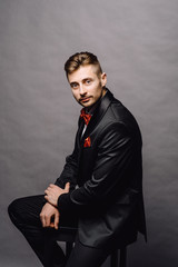 Fototapeta premium serious business man in elegant double breasted suit sitting on a chair on grey studio background
