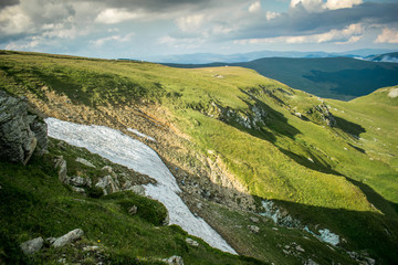 a beautiful mountain scenery. The heights of the mountains covered with grass and snow in July. A dramatic sky