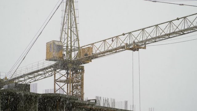 Working crane at construction site. Winter snowy weather. It is snowing. Strong wind