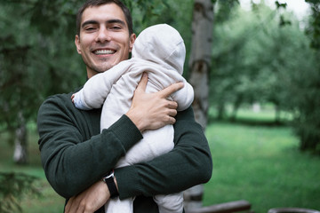 Naklejka na ściany i meble happy dad in green jacket hugs his baby in Park