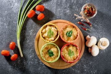 top view of casserole with baked cheese, chicken and mushrooms in cocoanuts with vegetables on gray background