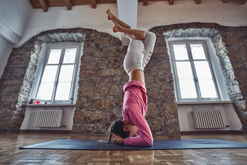 Young woman exercise yoga on a mat in the loft interior. Advanced asana.