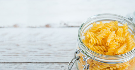 Macaroni in a glass jar on a wooden table on a light background. Cooking food. Close-up. The concept of vegetarianism and a balanced diet.