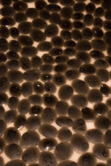 Abstract background with reflection of  water droplets on dark brown flat stones arranged in a random manner on the floor of a lighter shade.