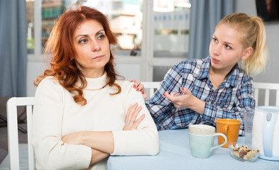 Mature female talking with young daughter at table in home
