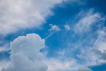 many fluffy clouds on a blue sky. The trace of a plane that enters in the clouds