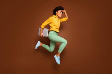 Fototapeta na wymiar Full body photo of funky dark skin lady jump high hold notebook hurry lessons school see building close wear yellow shirt green pants footwear isolated brown color background